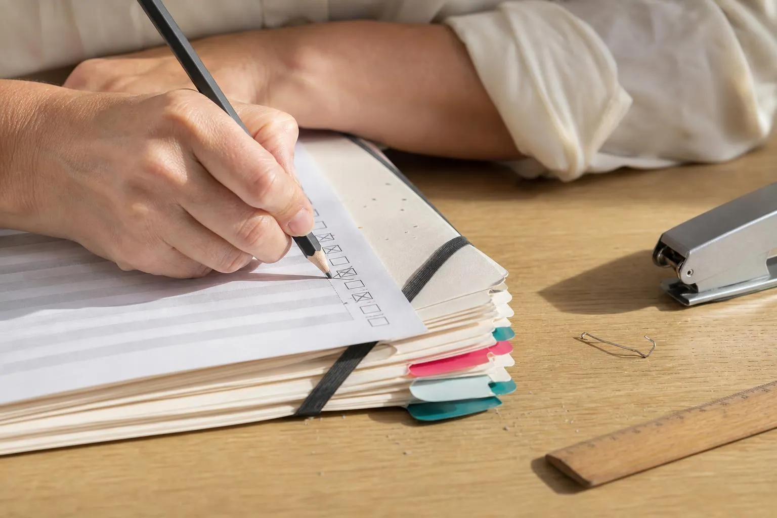 Gros plan de mains féminines cochant au crayon une liste de pièces posée sur des pochettes à rabats étiquetées et empilées